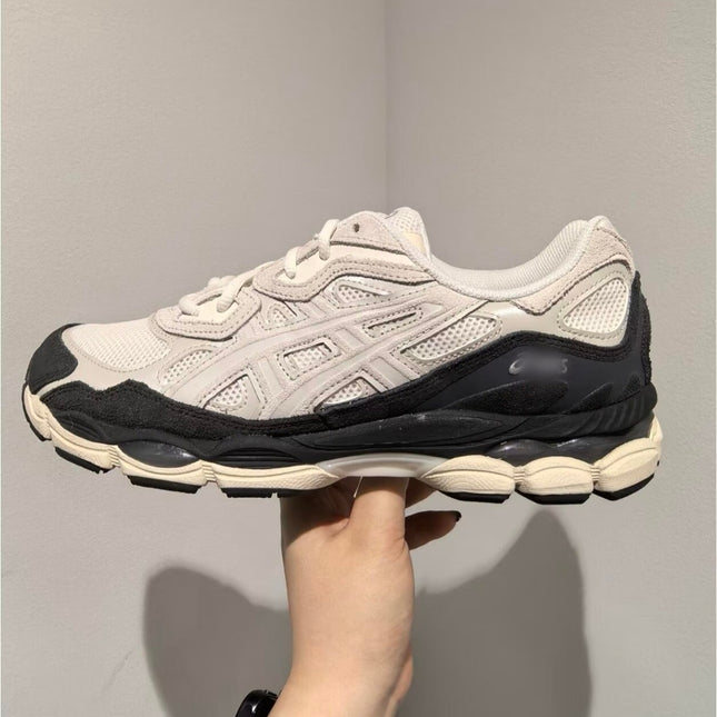 White sneaker with black accents, chunky sole, and mesh texture, held in a hand against a plain wall.