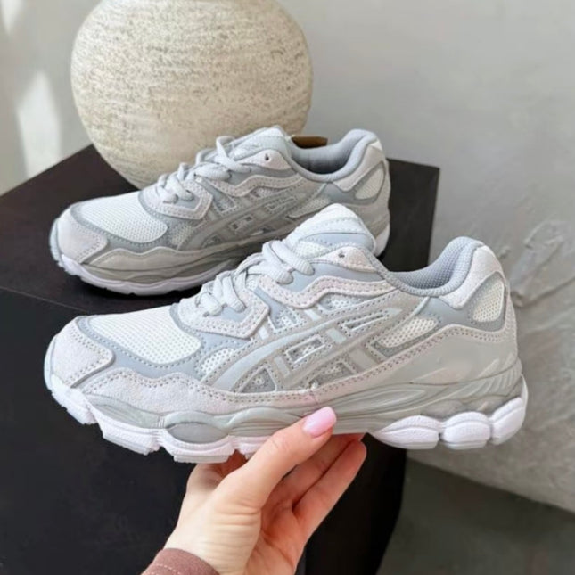 Gray and white sneakers with mesh and leather details on a dark surface, held by a hand.
