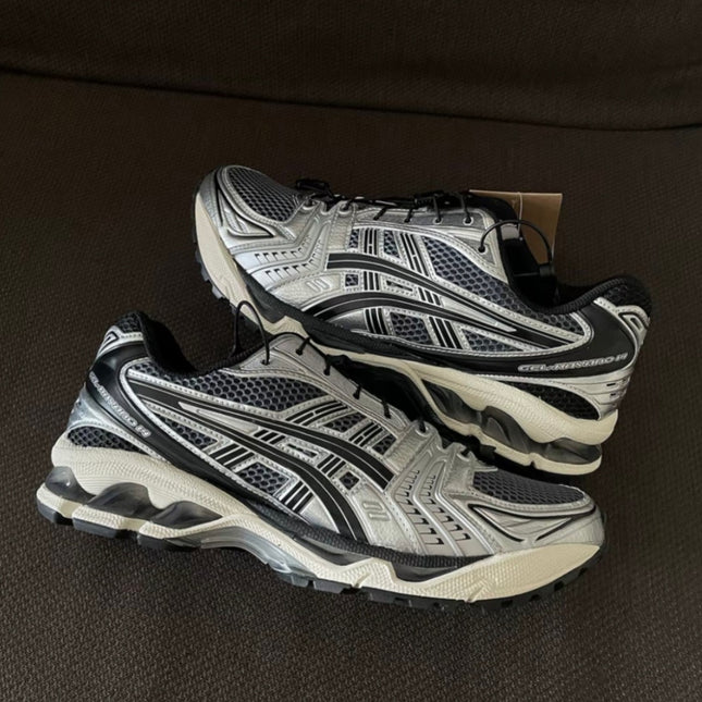 Silver and black running shoes with intricate patterns, black laces, and white soles on a dark surface.