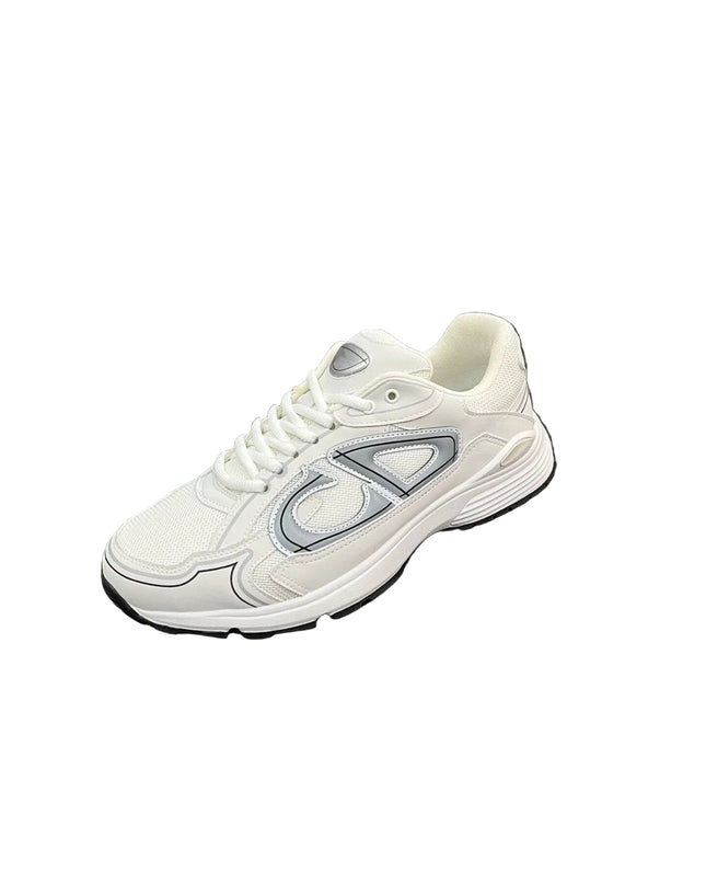 A white athletic sneaker with a large silver and gray side logo, displayed on a black textured suitcase against a background of silver curtains.