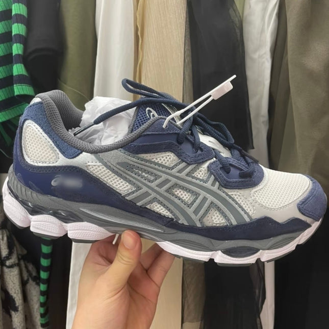 A navy and gray sneaker with white mesh, gray accents, and a white sole held by a hand.