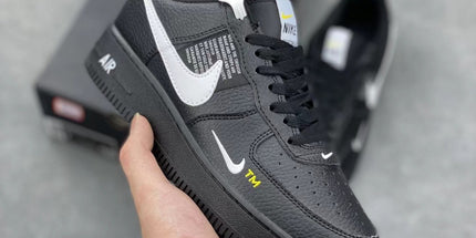 Black sneaker with white accents held by a hand on a gray background
