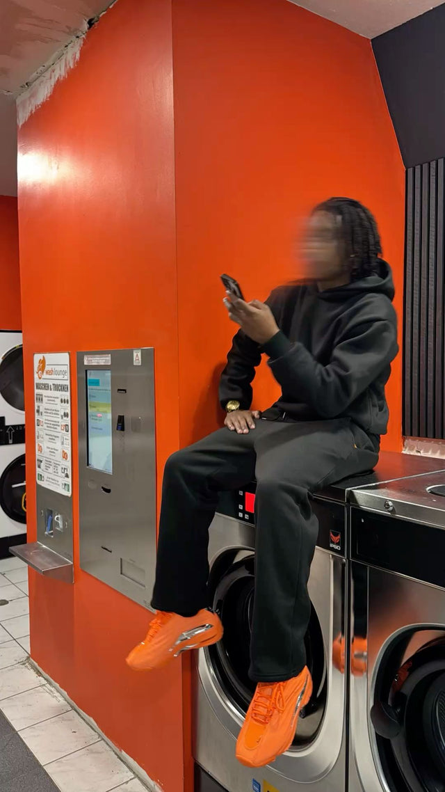 Black streetwear tracksuit with orange NOCTA Hot Step 2 sneakers